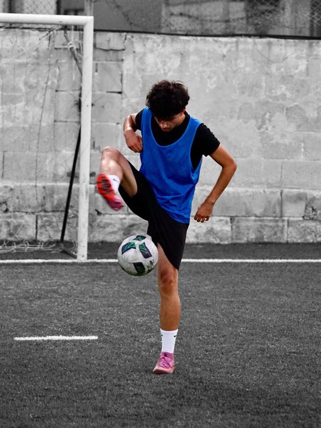 A player in a blue bib controlling the ball in front of the goal