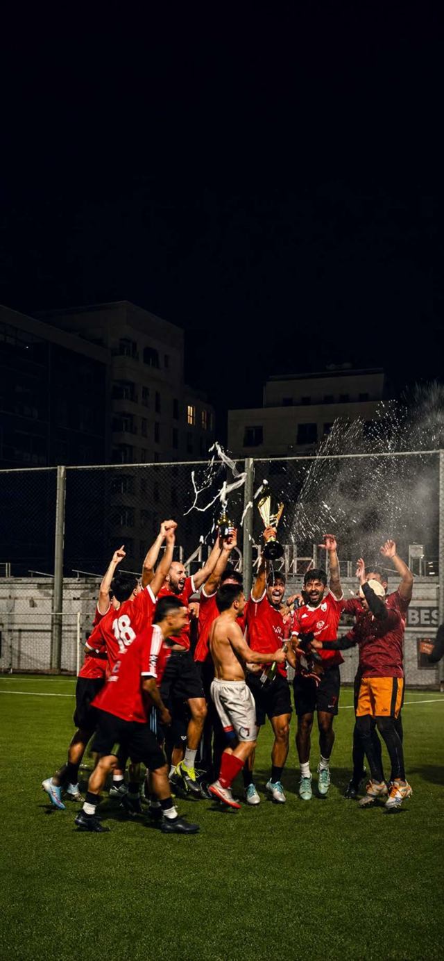 Players lifting a trophy and spraying a bottle at night
