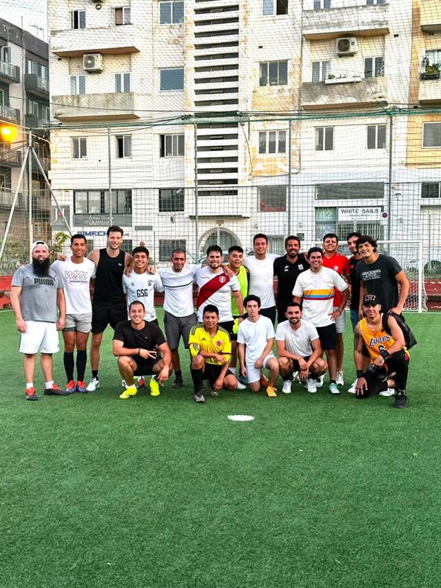 Around twenty players of many nationalities, arms around each other, after an evening game on a caged pitch in Malta