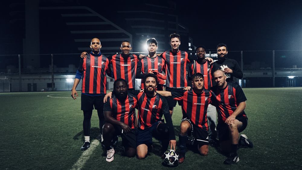 The Football Amigos FC squad in red and black stripes under floodlights